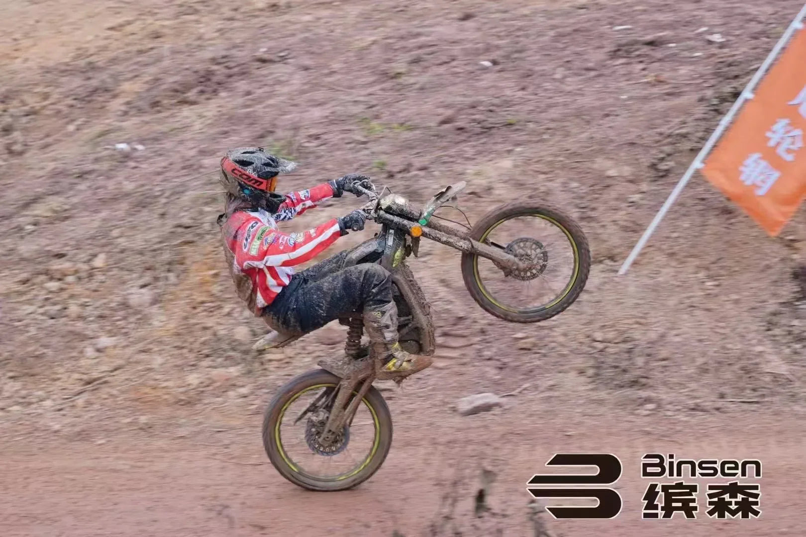 Person riding a dirt bike on a muddy track with 'Binsen' branding.