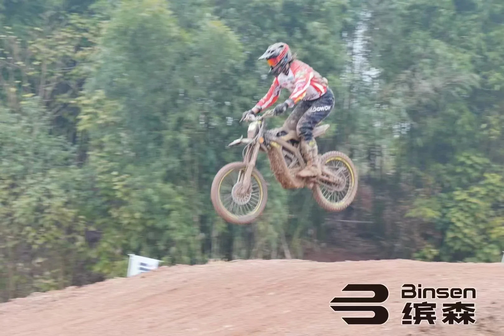Motocross rider in action on a dirt track with Binsen branding.