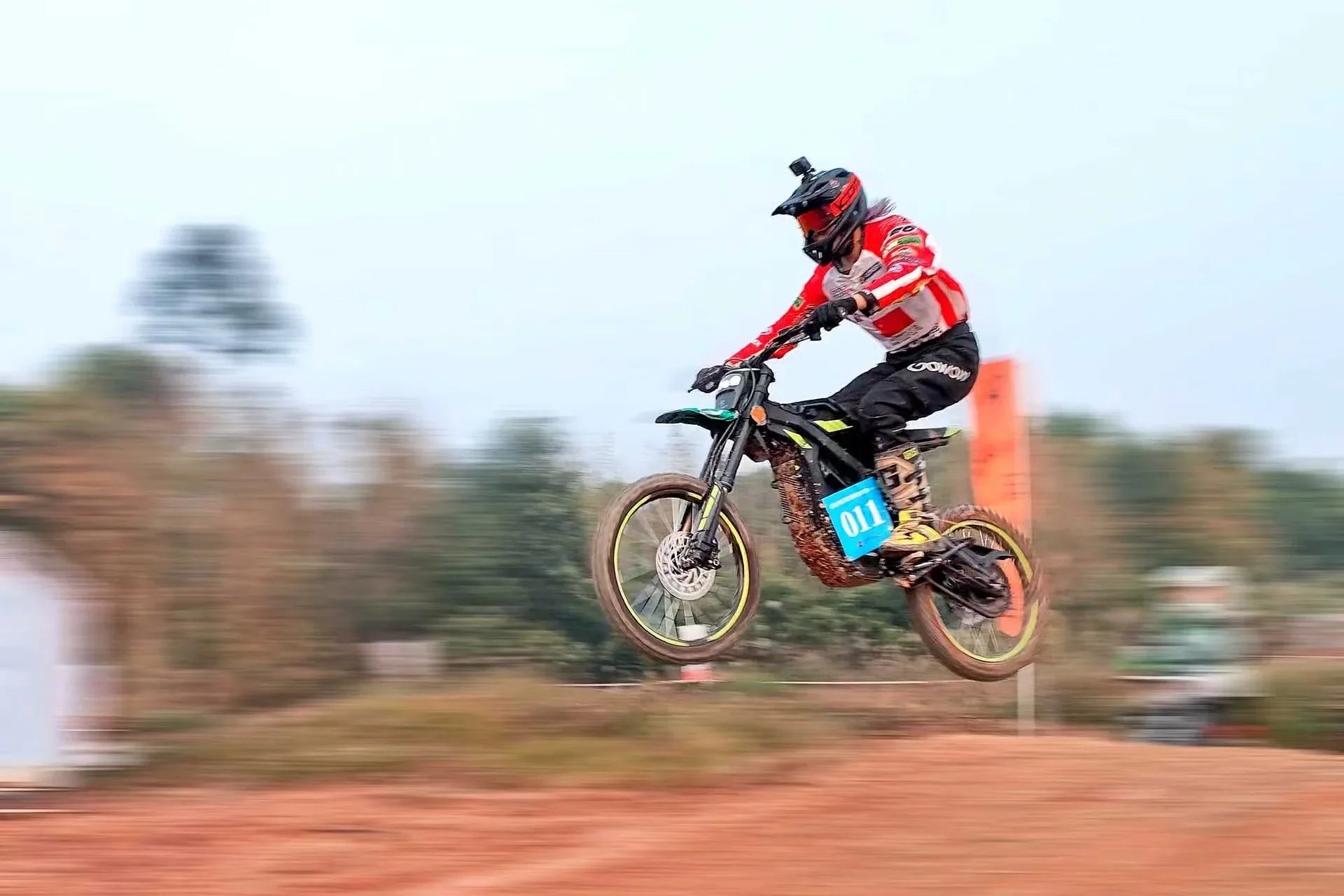 Biker in mid-air performing a stunt on a dirt track with trees in the background