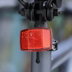 Red bicycle tail light attached to a bike frame with a blurred background