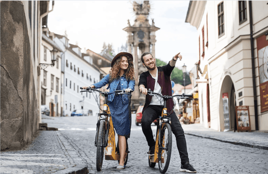 Young couple riding electric bikes in a European city street, enjoying Pogo Cycles e bikes