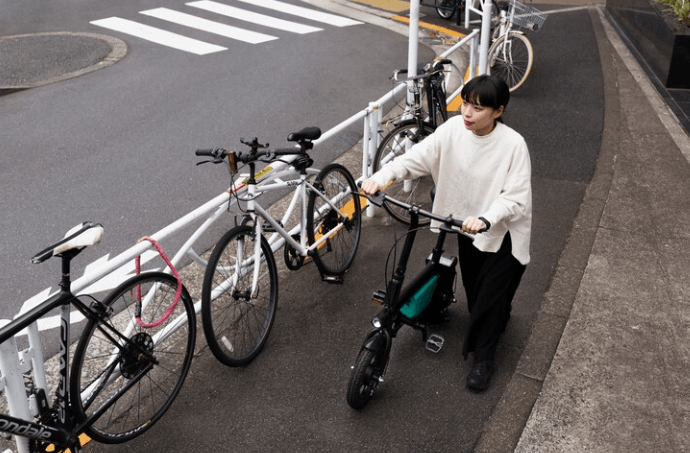 woman walking a compact electric bike with a green frame on a city sidewalk