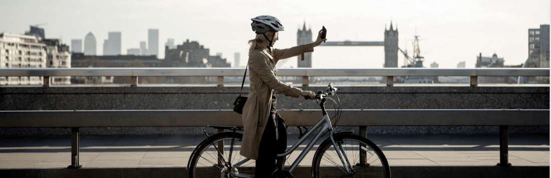 Woman in helmet with step-thru electric bike on city bridge, London skyline and Tower Bridge in background, Pogo Cycles