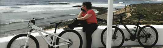 Person with two electric bikes overlooking ocean view, Pogo Cycles Ireland e-bike store